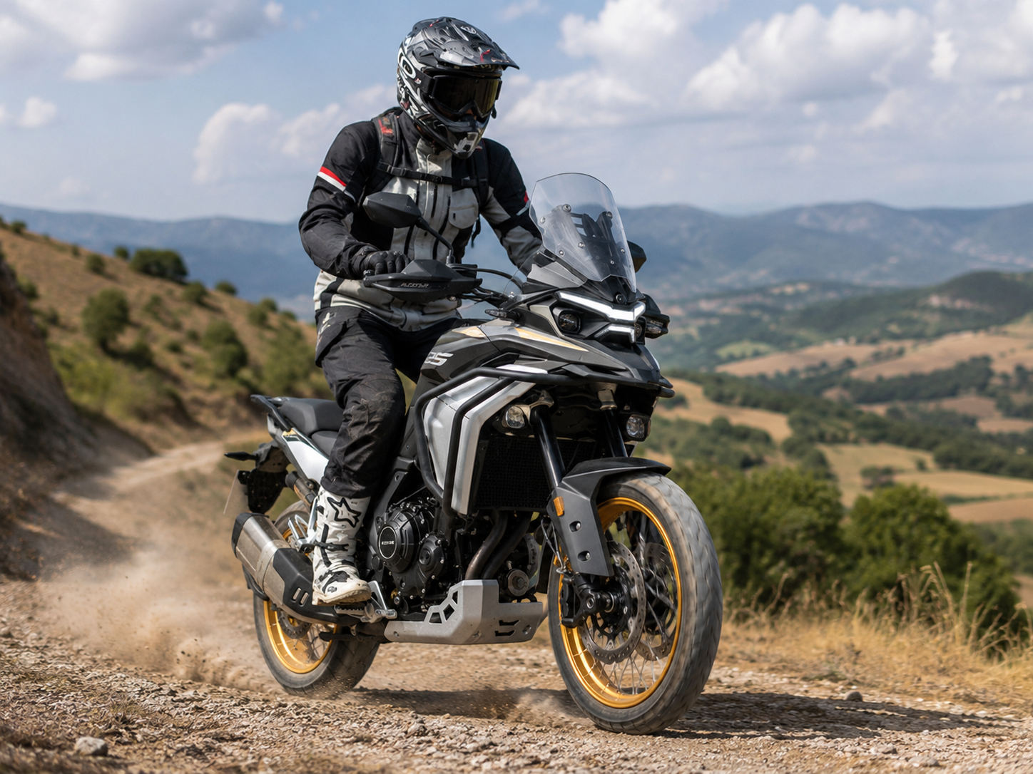 Motociclista conduciendo la Kove 625X por un camino de tierra en la montaña, levantando polvo